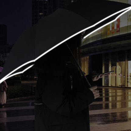 Person holding a dark umbrella with illuminated lines against a city street at night.