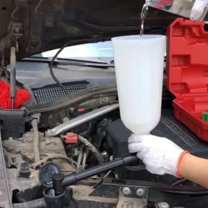 Person pouring liquid from a white funnel into a car's engine bay with a red toolbox in the background.
