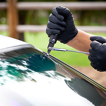 Person wearing black gloves using a tool on a car window
