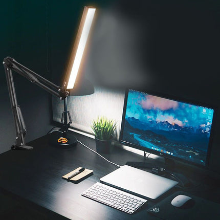 Dark office desk with a computer setup, including a monitor, keyboard, and lamp.