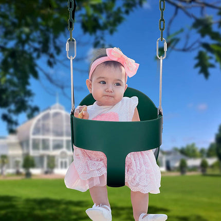Child in a green swing set with a clear blue sky and trees in the background
