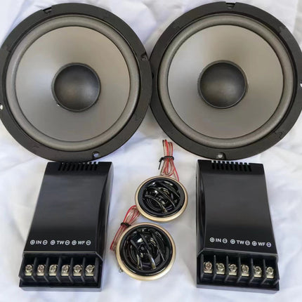 A pair of large black and gray car speakers with matching black amplifier modules and two smaller tweeters arranged on a white fabric background.