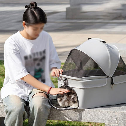 Person sitting on a bench with a pet carrier and a cat inside, outdoors.