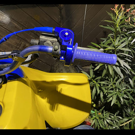 Close-up of a yellow and blue motorcycle handlebar with greenery in the background
