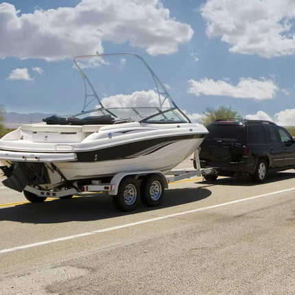 Boat on a trailer being towed by a car on a road with a clear sky.