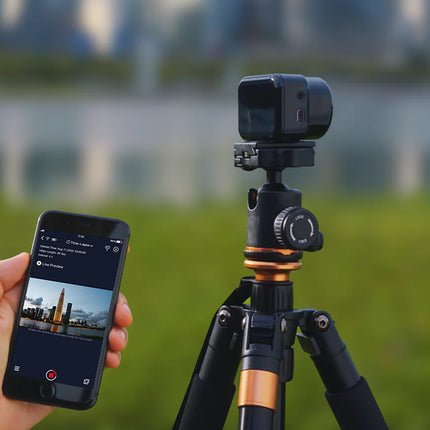 Person using a smartphone to control a camera on a tripod outdoors.