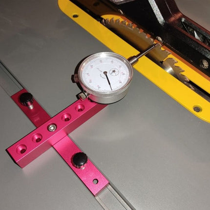 A bright pink aluminum square with a dial indicator and a silver straightedge ruler, shown on a gray metal surface next to a yellow guide.