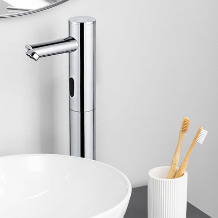 A modern chrome single-handle sink faucet installed above a white vessel sink, with a white toothbrush holder and two bamboo toothbrushes on the right against a light gray wall.
