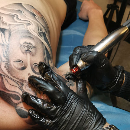 Person getting a tattoo of a Buddha design on their arm.