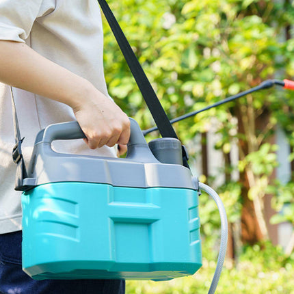 A person outdoors holding a teal and gray backpack sprayer with a black shoulder strap and wand, with green foliage in the background.