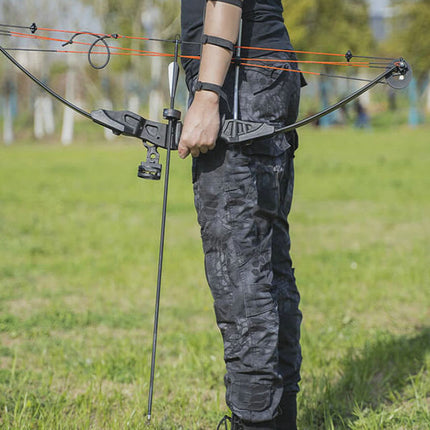 Person holding a crossbow in an outdoor setting with grass and trees in the background