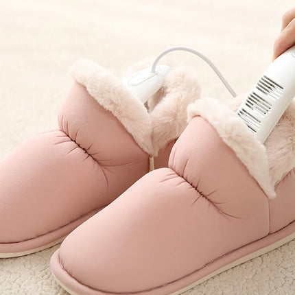 Pink slippers with white fur lining being heated by a handheld electric device.