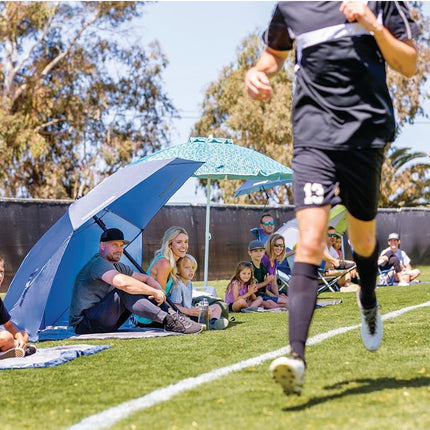Soccer game in progress with players on a field and spectators under umbrellas.