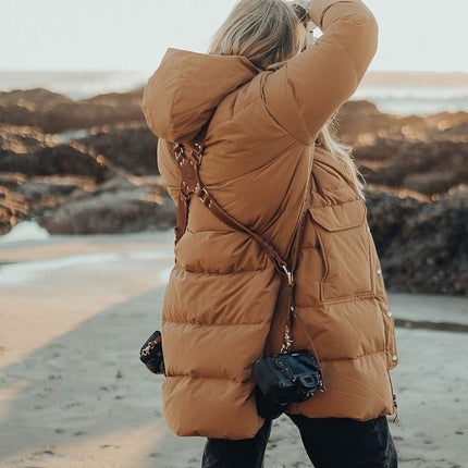 Person in a brown puffer coat on a beach with another person partially visible