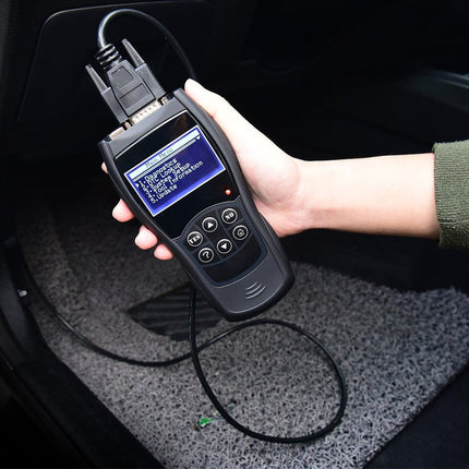 Hand holding a diagnostic tool connected to a car's OBD2 port inside a vehicle.
