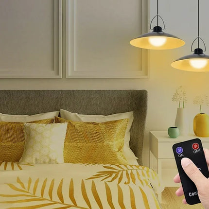 Hand holding a remote control over a bed with yellow and white bedding in a bedroom setting.