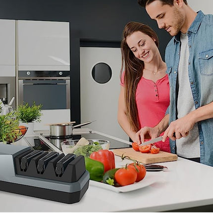 A countertop kitchen scene with a man and woman slicing vegetables at a cutting board, while a gray and black sharpness trainer device sits on the counter in the foreground.