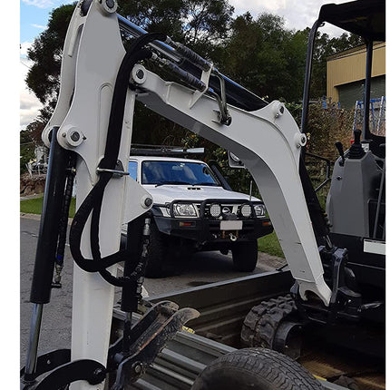 A close-up of a white and black compact excavator or skid steer with hydraulic arms, photographed outdoors next to a white pickup truck on a paved surface.