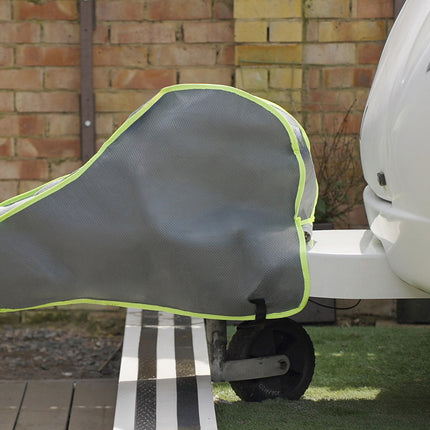 Gray saddle cover with green trim attached to a vehicle, against a brick wall background.