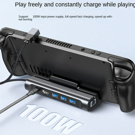A black 100W USB-C gaming accessory dock with dual game controllers attached, shown on a light blue background with promotional text and a large '100W' graphic.