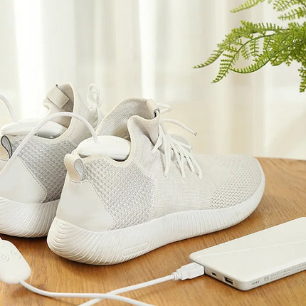 White sneakers with charging cable on a wooden surface with a plant in the background