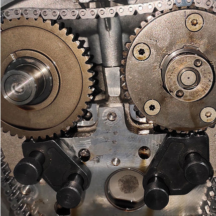 Close-up of a mechanical gear system with two large metal sprocket gears, a chain, and black plastic or metal adjustment components on a worn metallic housing.
