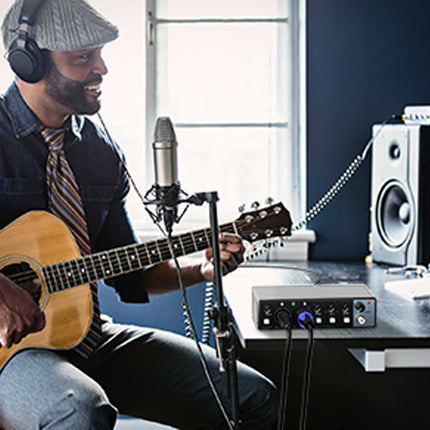 Man playing guitar in a home studio with microphone and speakers.