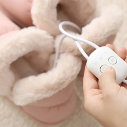 Hand holding a white electronic device with buttons near a fluffy beige blanket