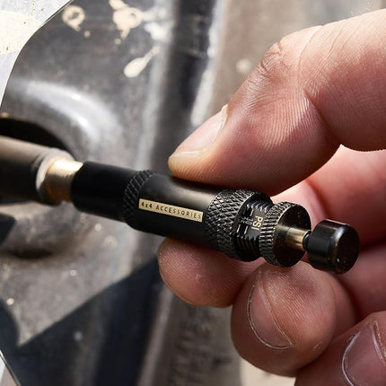 A close-up of a hand holding a black and gold 3M Accessory dial tool against a dark metallic background.