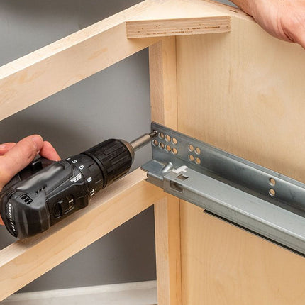 Person using a drill to assemble a wooden shelf with metal brackets.