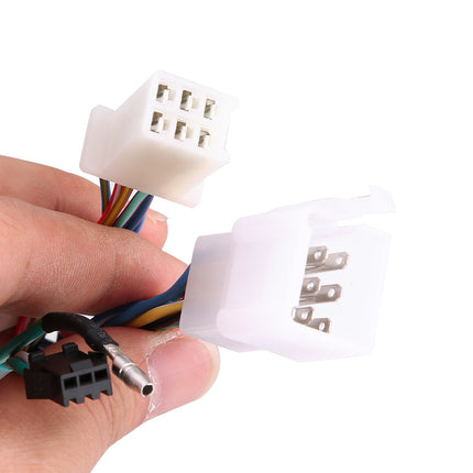A hand holding two white plastic multi-pin electrical connector plugs with attached multicolored wires and a small black connector, shown against a plain white background.