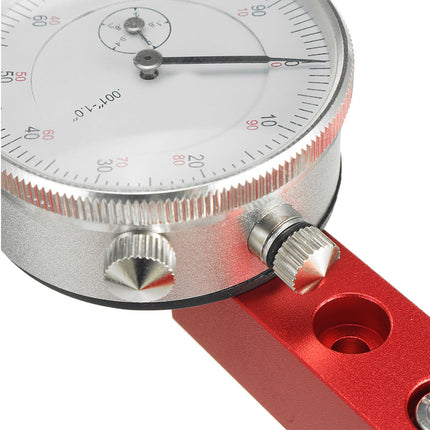 Close-up of a precision dial indicator or angle gauge with a silver metallic dial housing, black needle, red measurement markings, and a red anodized handle on a white background.