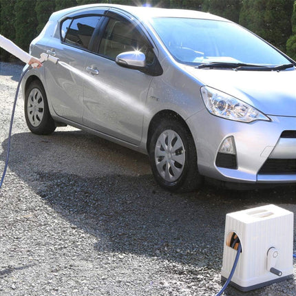 Silver car being charged with a charging cable on a gravel surface.