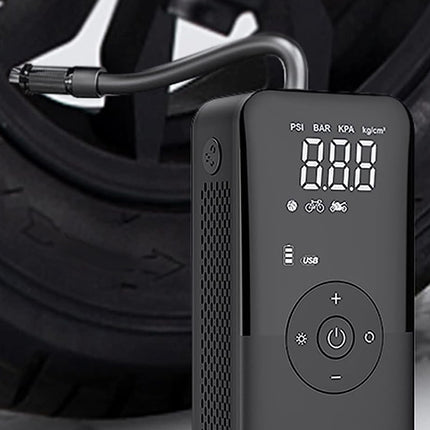 A black digital tire inflator with a hose attached, shown in front of a blurred car tire. The device has a digital display screen and control buttons.