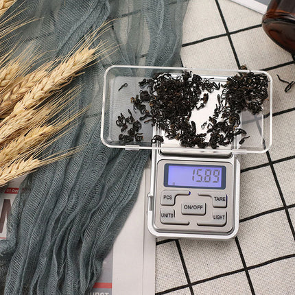 Digital scale with black seeds on a checkered surface with dried plants.