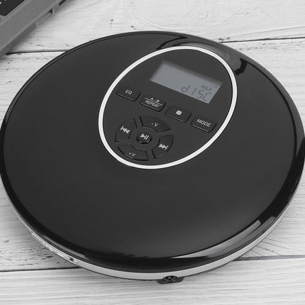 A black round CD player with a digital display and control buttons, resting on a white wooden surface.
