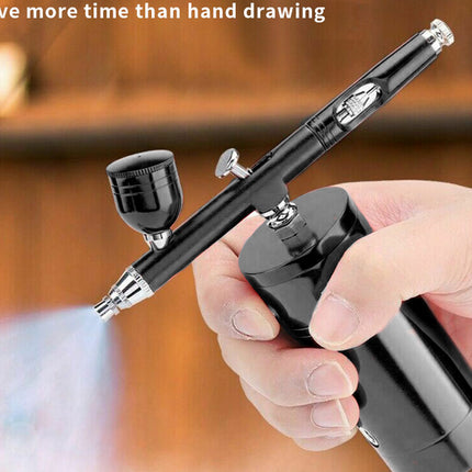 A handheld black airbrush pen with a cylindrical battery or tank, shown being held by a person's hand. The product has silver metal accents and a spray nozzle with a visible mist output.