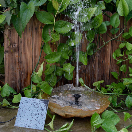 Small water fountain surrounded by greenery with a wooden background