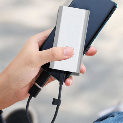 Hand holding a smartphone with a power bank attached, blurred background