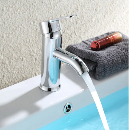 Chrome faucet with soap dispenser on a sink with a towel and bottle in the background.