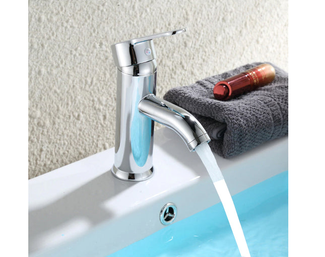 Chrome faucet with soap dispenser on a sink with a towel and bottle in the background.