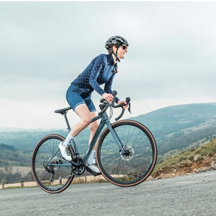 Person riding a bicycle on a road with mountains in the background