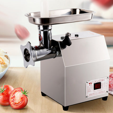 Stainless steel meat grinder on a wooden surface with tomatoes and ground meat in the background