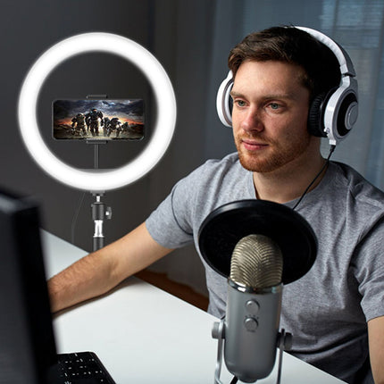 Man with headphones and microphone setup in front of a computer screen with a ring light.