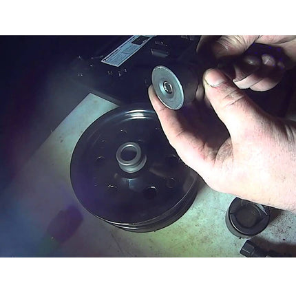 Person holding a small metal component next to a larger mechanical part on a workshop bench.
