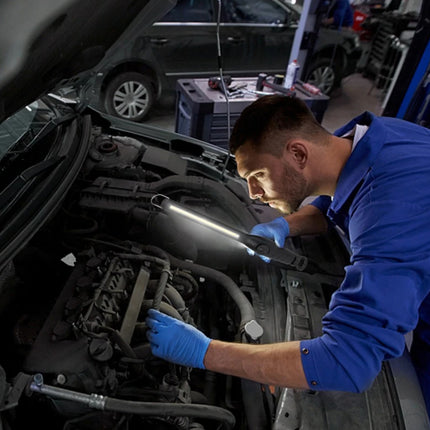 Mechanic working on a car engine with tools and equipment in the background