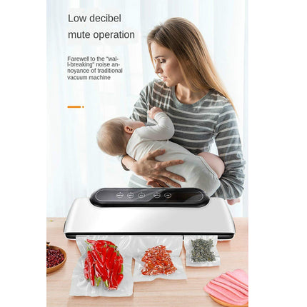 Woman holding a baby next to a vacuum sealing machine with food packaging on a table.