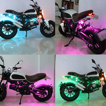 A four-panel collage showing a small motorcycle in different lighting color modes: blue rear light, pink rear light, purple/magenta lighting, and green rear light. The motorcycle itself appears black and white, photographed indoors against plain walls.