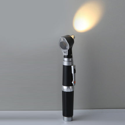 A handheld medical ophthalmoscope with a black and silver body, standing upright on a white surface against a gray background, with its light turned on casting a warm yellow glow.
