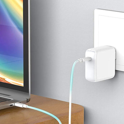 Laptop connected to a power adapter on a wooden surface with a light gray wall in the background.